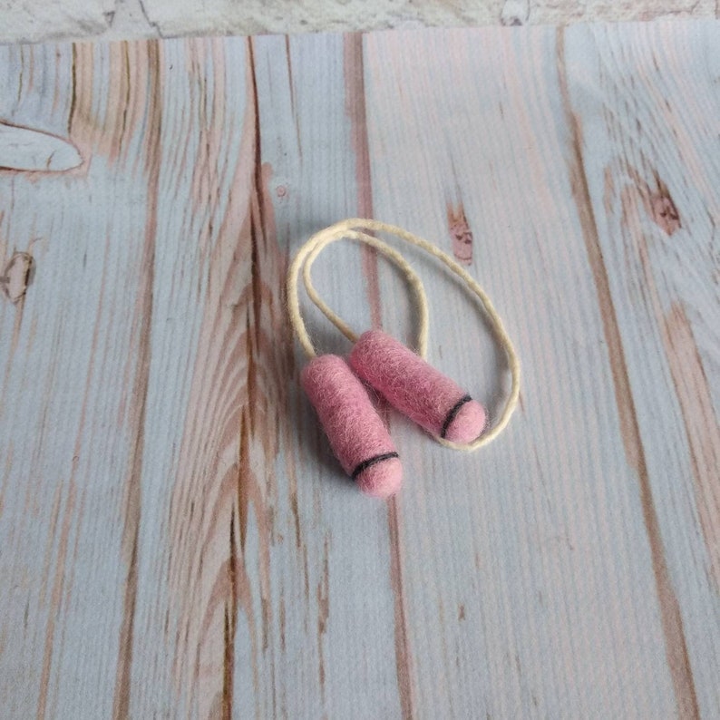 May include: A pink felt jump rope with white string. The jump rope is on a light wood background.