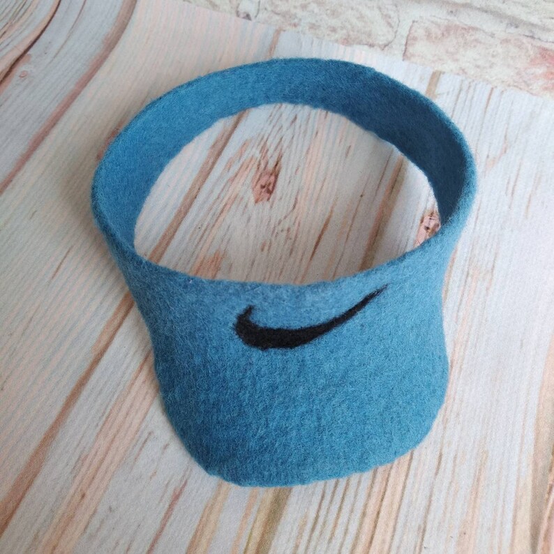 K&ouml;nnte beinhalten: Ein blauer Filz-Visier mit einem schwarzen Nike-Swoosh-Logo.