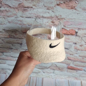 May include: A beige felt wine glass cozy with a black Nike swoosh logo.