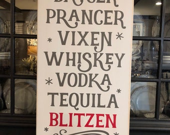 May include: A white wooden sign with the names of the reindeer from the song "Rudolph the Red-Nosed Reindeer" replaced with alcoholic beverages. The sign reads: * Dasher * Dancer * Prancer * Vixen * Whiskey * Vodka Tequila Blitzen * * *&