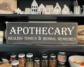 May include: A black wooden sign with white lettering that reads "Apothecary Healing Tonics & Herbal Remedies".