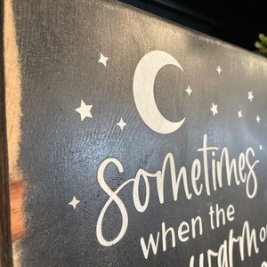 Op de afbeelding: Een zwart houten bord met een witte halve maan en sterren. Het bord staat "Sometimes when the world is warm..."