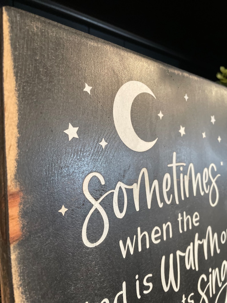 Op de afbeelding: Een zwart houten bord met een witte halve maan en sterren. Het bord staat "Sometimes when the world is warm..."