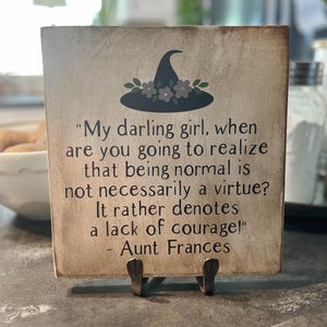 May include: Aged-look wooden sign with a witch hat illustration and the quote "My darling girl, when are you going to realize that being normal is not necessarily a virtue? It rather denotes a lack of courage!" - Aunt Frances.