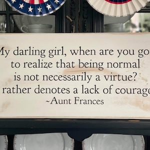 May include: White wooden sign with a black painted quote: "My darling girl, when are you going to realize that being normal is not necessarily a virtue? It rather denotes a lack of courage." - Aunt Frances