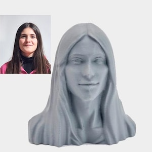 Pode incluir: Busto cinzento de uma mulher com cabelo comprido e um véu drapeado. A escultura tem uma expressão serena. Uma pequena foto de uma mulher está no canto superior esquerdo.
