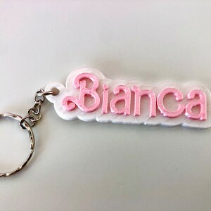 Può includere: Un portachiavi bianco con un'etichetta nome stampata in 3D rosa che dice "Bianca" e un anello portachiavi argentato.