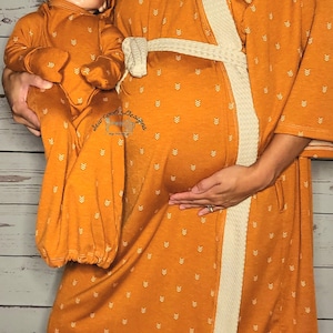 May include: A matching set of orange and white patterned robes for a parent and baby. The robes have a white sash and are made of a soft, comfortable fabric.