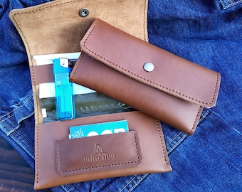 May include: A brown leather wallet with a flap closure and a separate pocket for a lighter. The wallet is open and has a blue lighter inside. The wallet has the text "Leather Style" embossed on the front.