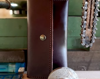 May include: A brown leather key holder with a snap closure. The key holder is sitting on a wooden surface.