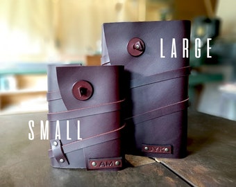 May include: Two leather-bound journals, one labeled "SMALL" and the other "LARGE". Both journals are dark purple with brown leather straps and metal accents.