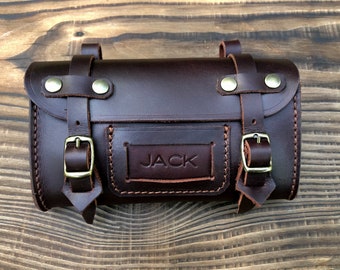May include: A brown leather bicycle handlebar bag with a brass buckle and the name "JACK" embossed on the front.