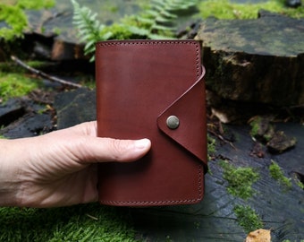May include: A brown leather notebook cover with a flap closure and a metal button. The cover has a stitched edge and a subtle textured finish.