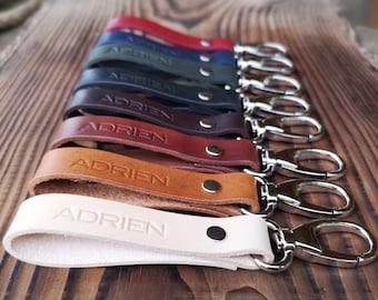 May include: A set of eight leather keychains with a silver key ring. Each keychain is a different color and has the name "Adrien" embossed on it.