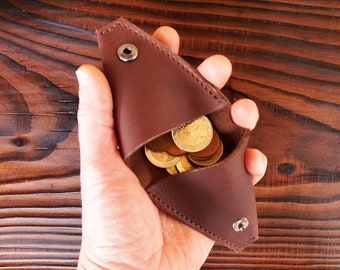 May include: A brown leather coin purse with a flap closure and a snap button. The purse is open and filled with gold coins.