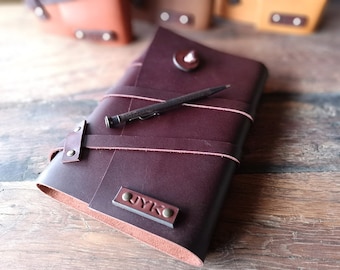 May include: A dark brown leather journal with a pen and a metal button closure. The journal has a personalized name tag that says "UYKO".