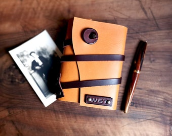 May include: A brown leather journal with a tan cover and brown leather straps. The journal has a metal button closure and the initials "WST" are embossed on the front cover.
