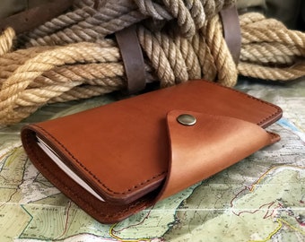 May include: A brown leather wallet with a flap closure and a metal button. The wallet is lying on a map.