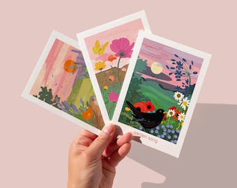 Peut inclure: Trois cartes illustrées sur le thème de la nature. La première carte représente un paysage de coucher de soleil avec un oiseau volant au-dessus d'un champ de fleurs. La deuxième carte représente un papillon volant au-dessus d'un champ de fleurs. La troisième carte représente un merle noir perché sur une branche dans un champ de fleurs. Le texte "garden song" est imprimé en bas de la troisième carte.