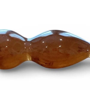May include: A brown, elongated massage tool with a smooth, glossy finish. The tool has a bulbous end and a cluster of rounded protrusions on the opposite end. The shape is ergonomic, designed for ease of use.