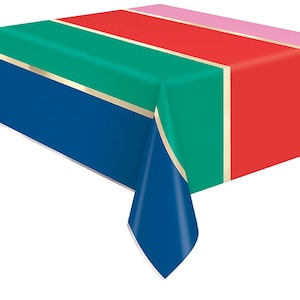 May include: A colorful rectangular tablecloth with a striped design. The stripes include blue, green, red, and pink, separated by gold trim. The tablecloth is folded over a surface, with a corner hanging down.