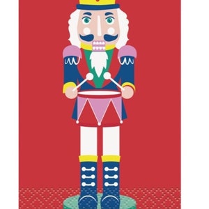 May include: A colorful illustration of a nutcracker soldier playing a drum. The nutcracker wears a yellow hat, blue jacket, and red skirt. The background is red with a gold border.