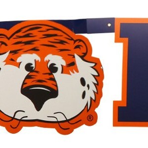 May include: A banner with the words "WAR EAGLE" in orange and navy blue block letters. A cartoon tiger mascot is featured in the center and at the end of the banner. The banner is likely for Auburn University.