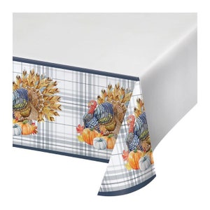 May include: A white tablecloth with a plaid pattern featuring turkeys, pumpkins, and fall leaves. The border is a dark blue. The tablecloth is designed for Thanksgiving or autumn gatherings.