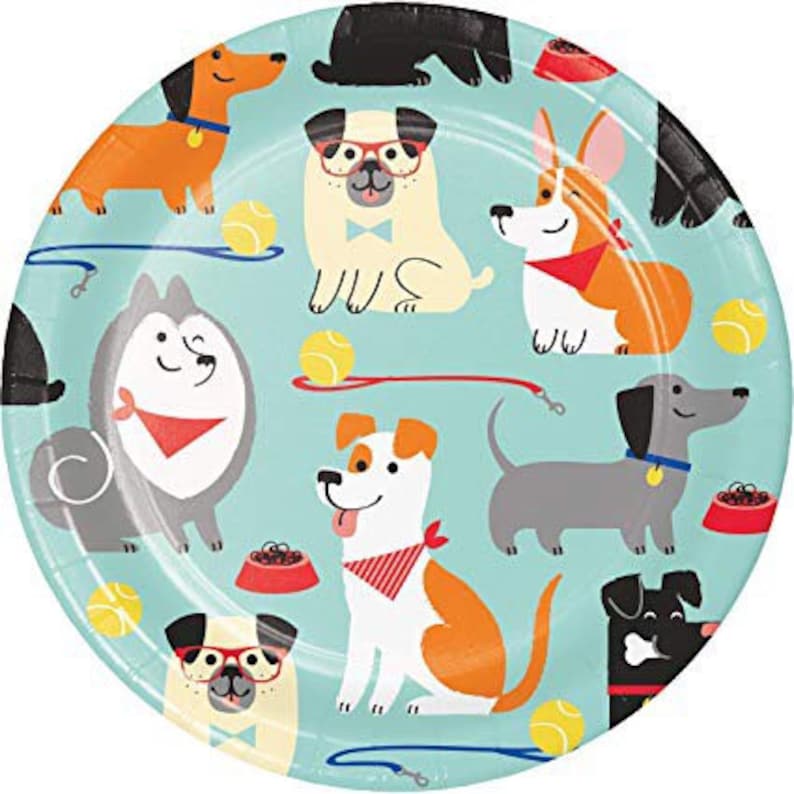 May include: A round, light blue paper plate featuring various cartoon dog illustrations. The dogs are in different breeds and colors, with tennis balls, leashes, and food bowls scattered around the plate.