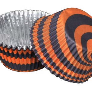 May include: Two cupcake liners with a black and orange striped design. The interior of the liners is silver. The liners are made of paper and are designed to hold cupcakes or muffins.