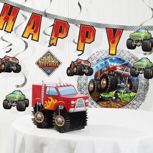 May include: A red monster truck centerpiece with flame decals and black wheels sits on a white table. The background includes a banner that says "HAPPY" and other monster truck decorations. A "Happy Birthday" sign is also visible.
