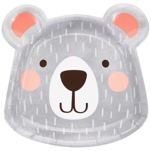 May include: A gray paper plate shaped like a bear's face, with a white snout, brown nose, and pink ears and cheeks. The plate has a textured surface with white vertical lines, and is designed for a children's party.