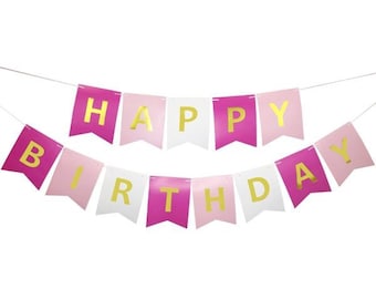 May include: A festive banner with the words "HAPPY BIRTHDAY" spelled out on colorful pennants. The pennants are in shades of pink, white, and magenta, with gold lettering. The banner is strung on a thin white string.