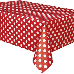 May include: A red tablecloth with a white polka dot pattern. The tablecloth is rectangular and covers a table. The polka dots are evenly spaced across the surface. The tablecloth is made of a smooth material.