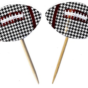 May include: Two football-shaped cupcake toppers. Each has a black and white houndstooth pattern with a brown center and white laces. The toppers are attached to wooden sticks, perfect for a sports-themed party.