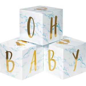 May include: Three white marble-patterned blocks spelling "BABY" in gold letters. Each block has gold footprints and blue veining. The blocks are stacked, creating a decorative display for a baby shower or nursery.