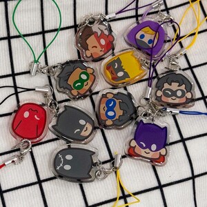 Peut inclure: Une collection de dix breloques en acrylique représentant des têtes de personnages de dessins animés stylisés, chacune attachée à une boucle en cordon de nylon coloré. Les motifs incluent des figures masquées aux couleurs vives, avec le texte WPPYART.