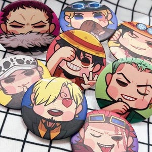 May include: A collection of round, colorful buttons featuring cartoon character illustrations. The buttons showcase various characters with distinct facial expressions and vibrant color schemes, set against a checkered background. The buttons are a fun, collectible item.
