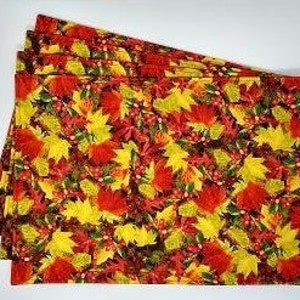 May include: Set of four placemats featuring a colorful autumn leaf pattern in shades of red, yellow, and green. The placemats are made of fabric and have a quilted texture.