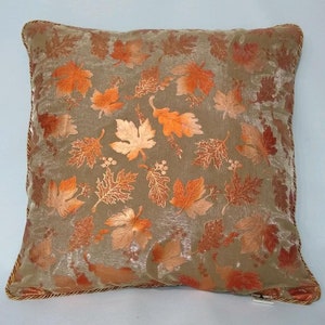 May include: A decorative throw pillow with a beige background and an embroidered pattern of orange and brown leaves.