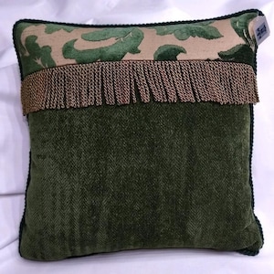 Puede incluir: Una almohada verde con ribete de flecos marrones y una tela estampada beige y verde en la parte superior. La almohada tiene un borde verde oscuro.