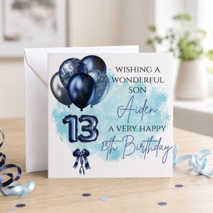 May include: A square birthday greeting card featuring a cluster of dark blue and silver balloons, the number 13 in balloon-style font, and a dark blue ribbon. The text reads: WISHING A WONDERFUL SON Aiden A VERY HAPPY 13th Birthday on a light blue background.