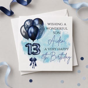 May include: A square greeting card featuring a cluster of dark blue and silver balloons, the number 13 in dark blue foil-style balloons, and a dark blue ribbon. The text reads: WISHING A WONDERFUL SON Aiden A VERY HAPPY 13th Birthday.