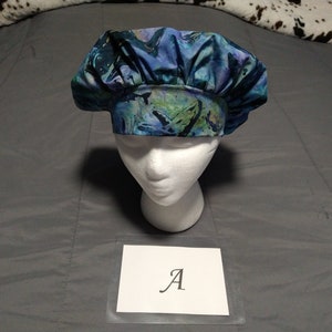 May include: A blue and green patterned surgical scrub hat with a white mannequin head. The hat has a tie at the back. The letter "A" is written on a white card in front of the hat.