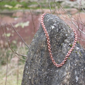 May include: A copper chain necklace draped over a rock. The chain is made of small, linked circles.
