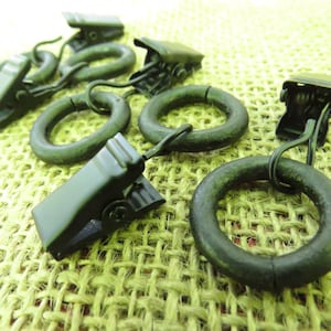 Puede incluir: Anillos de cortina de metal negro con clips. Los anillos tienen un diámetro de aproximadamente 3,8 cm y tienen un gancho en un lado. Los clips tienen aproximadamente 2,5 cm de largo y tienen un mecanismo de resorte.