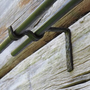 Op de afbeelding: Zwarte metalen dubbele gordijnroedebeugels gemonteerd op een houten muur. De beugels hebben een gehamerde afwerking en zijn ontworpen om twee roedes te dragen.