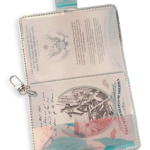 K&ouml;nnte beinhalten: Ein t&uuml;rkisfarbener Reisepasshalter mit einem transparenten Kunststoffeinsatz. Der Einsatz zeigt eine Vintage-Illustration eines Schiffes und den Text "O say does that star spangled banner yet wave O'er the land of the free and the home of the brave!" Der Halter zeigt auch den Text "AND THAT GOVERNMENT OF THE PEOPLE, BY THE PEOPLE, FOR THE PEOPLE, SHALL NOT PERISH FROM THE EARTH. ABRAHAM LINCOLN" und "THE UNITED STATES OF AMERICA".