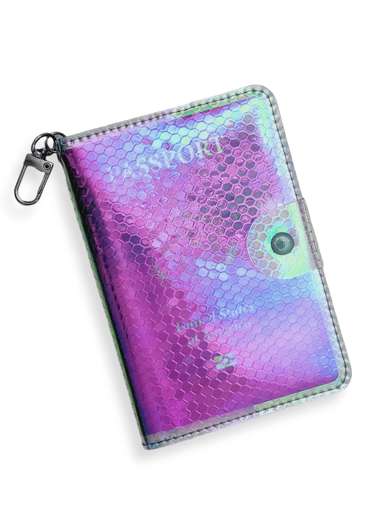 K&ouml;nnte beinhalten: Ein holografischer Reisepass-Etui mit einem Wabenmuster und einem silbernen Rei&szlig;verschluss. Das Etui hat ein transparentes Fenster, um den Reisepass anzuzeigen.