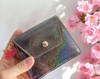 May include: A small black iridescent wallet with a gold button and a pink star charm attached to it.